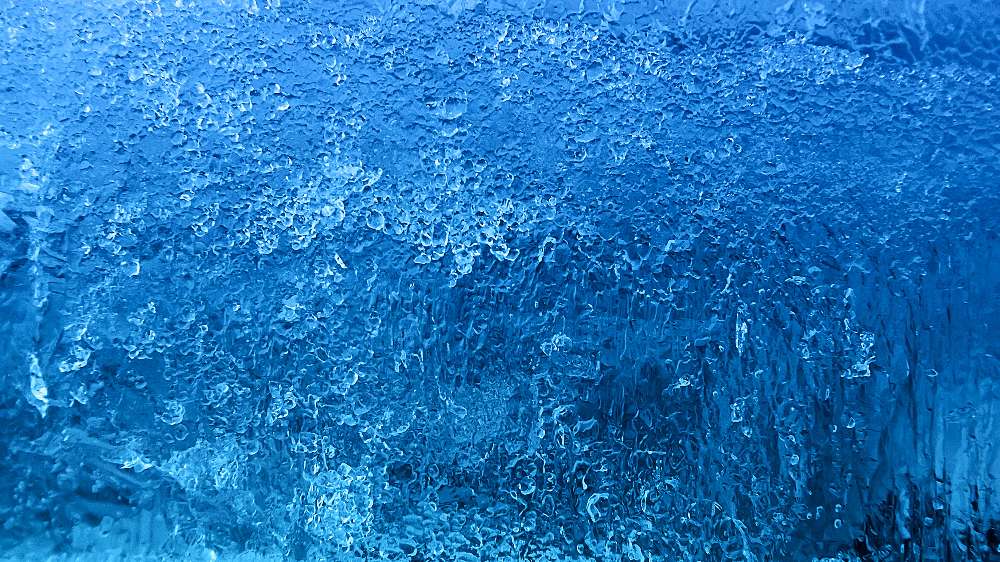 Close-up view of a textured ice surface, displaying various shades of blue and intricate patterns that resemble frozen air coils—similar to what you might see when air conditioner coil problems occur.
