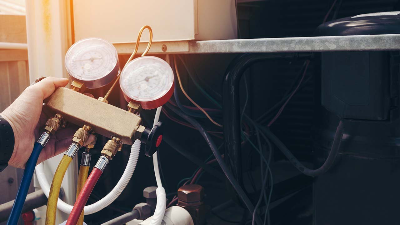 A person uses a manifold gauge set to check the pressure of an air conditioner, with various hoses connected to the equipment—even during Florida’s mild winter months.