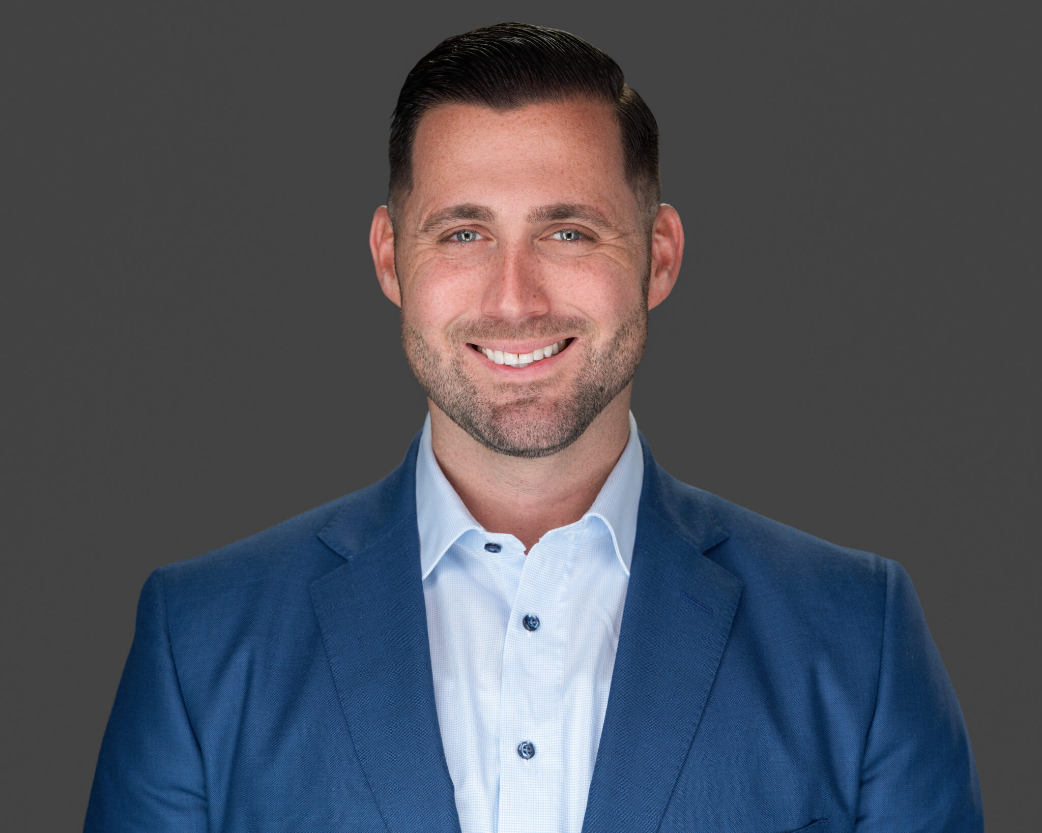 Anthony Perera, Entrepreneur of The Year Florida, smiles at the camera in a blue suit jacket and white shirt against a plain gray background.