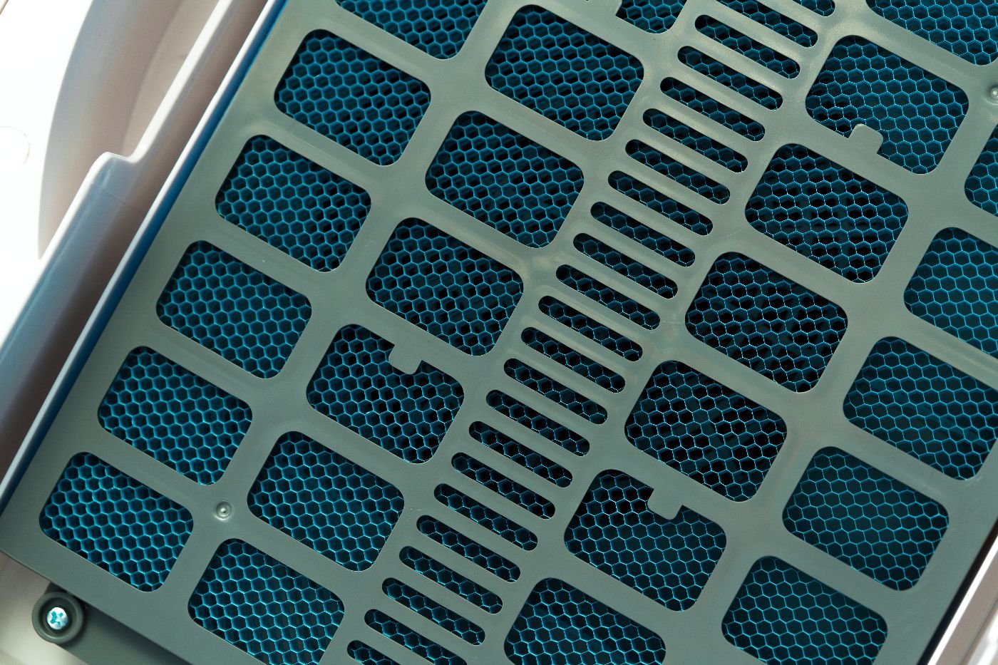 Close-up of a plastic grid cover over a blue honeycomb-like filter, possibly part of an air purifier or ventilation system designed to trap bacteria and other pathogens.