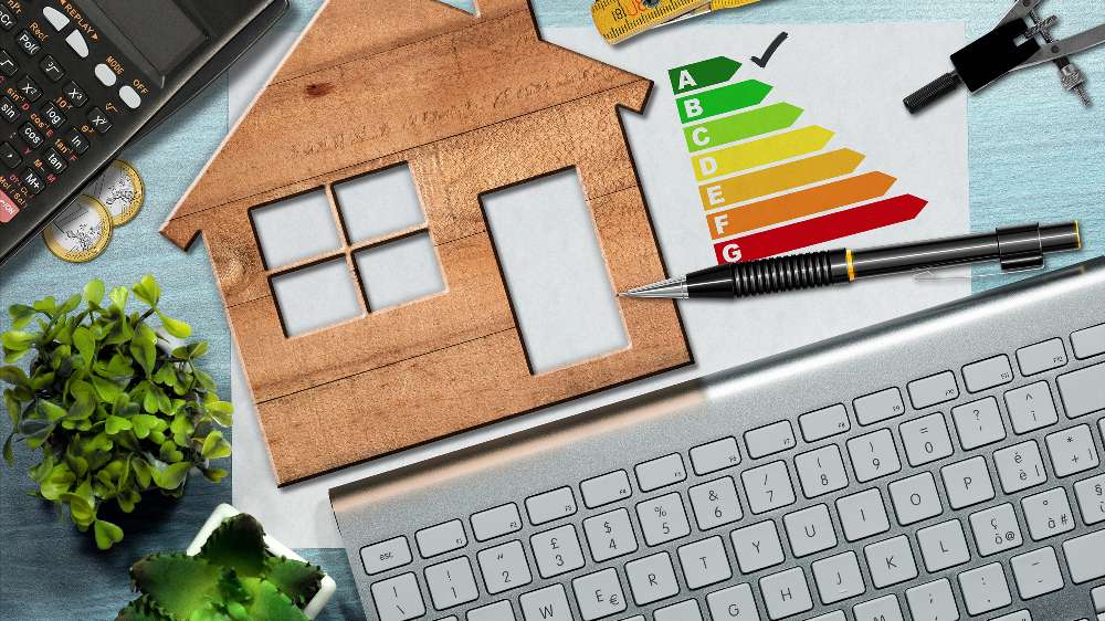 Wooden house cutout, energy efficiency rating chart, pen, calculator, plant, and computer keyboard on a table—highlighting the benefits of an energy-efficient AC for smarter home energy use.