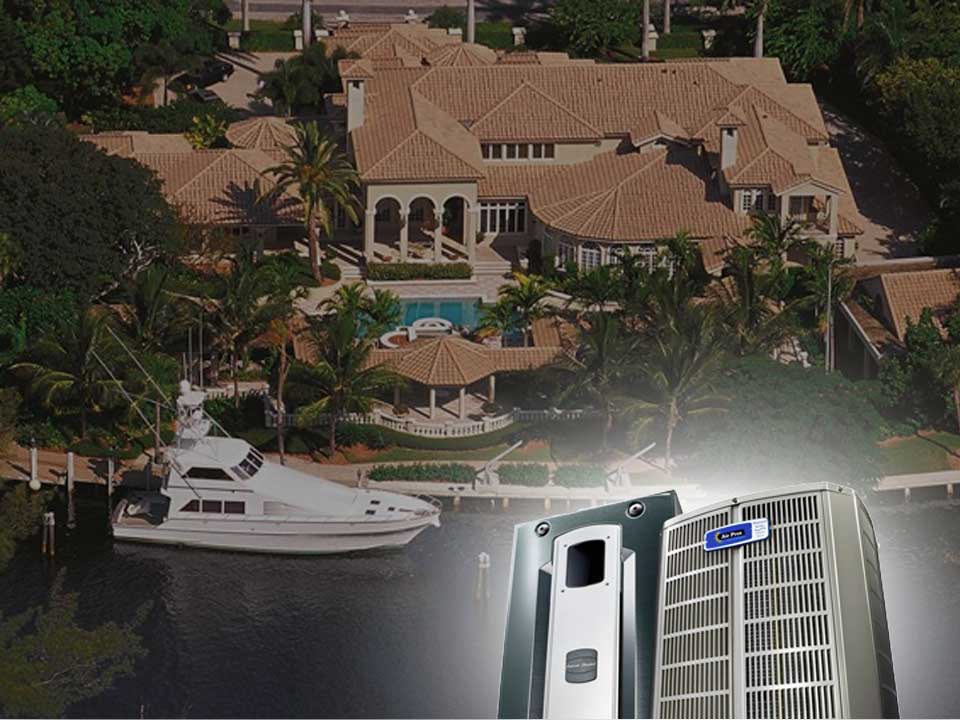A large waterfront house with a yacht docked outside, viewed from above, showcases world class status with two air conditioning units prominently displayed in the foreground.