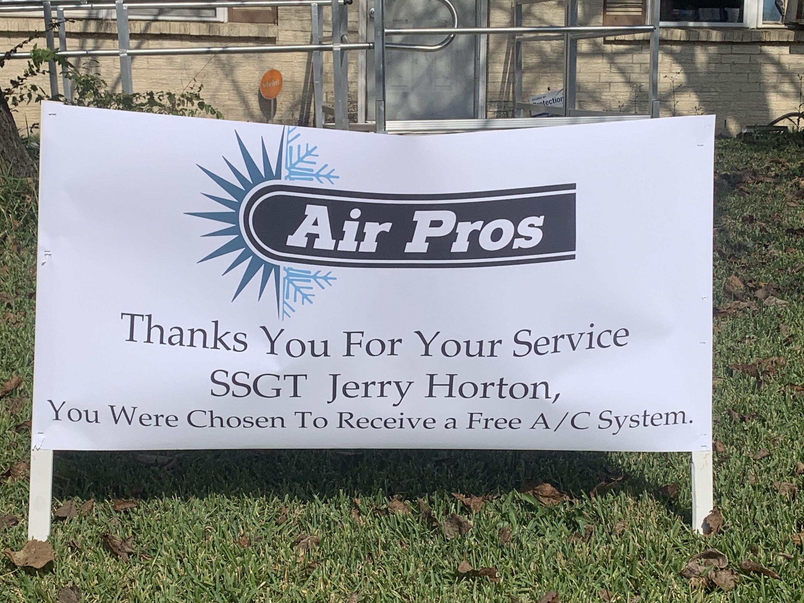 A sign on grass reads: "Air Pros USA. Thanks You For Your Service SSGT Jerry Horton of Balch Springs, You Were Chosen To Receive a Free A/C System.