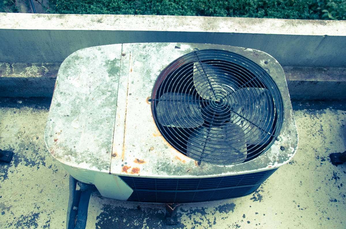 A weathered and rusty outdoor AC unit sits on a concrete surface next to a wall, viewed from above—highlighting the importance of preventing mold growth in aging air conditioning systems.
