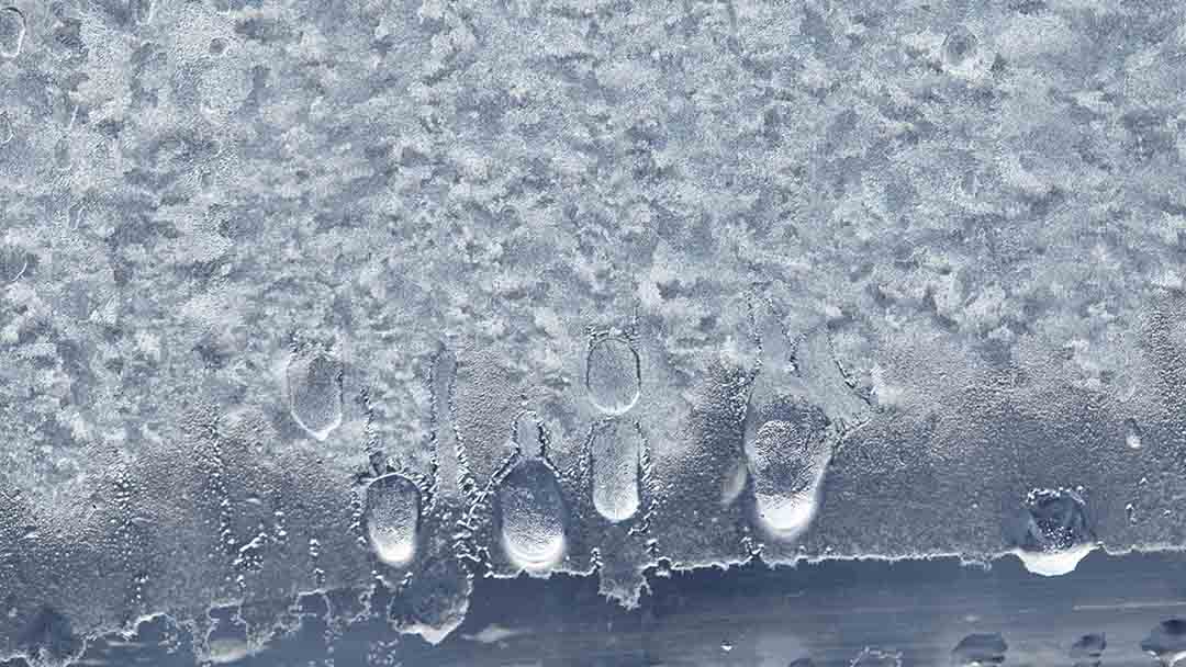 Close-up of melting ice with water droplets forming and running down a rough, frosty surface—a visual reminder of reasons for AC freezing and how easily air conditioner freezing can occur.