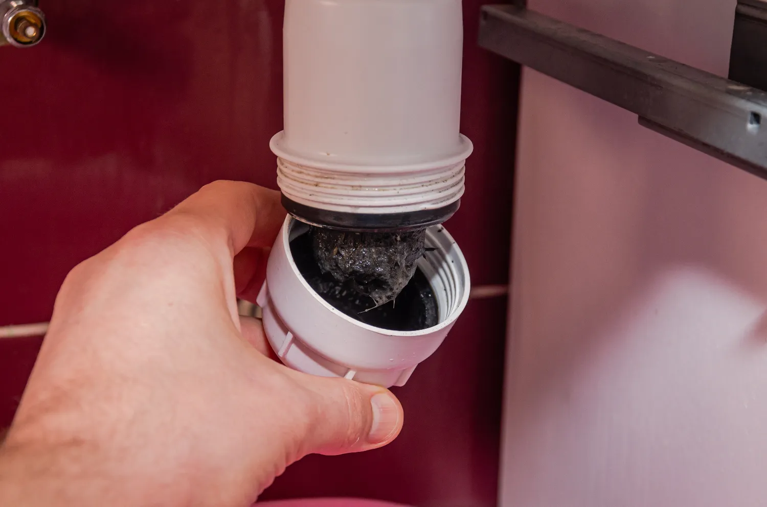 A hand holding a drain trap removed from a pipe, showing a buildup of black sludge and debris inside—highlighting the importance of regular drain cleaning.